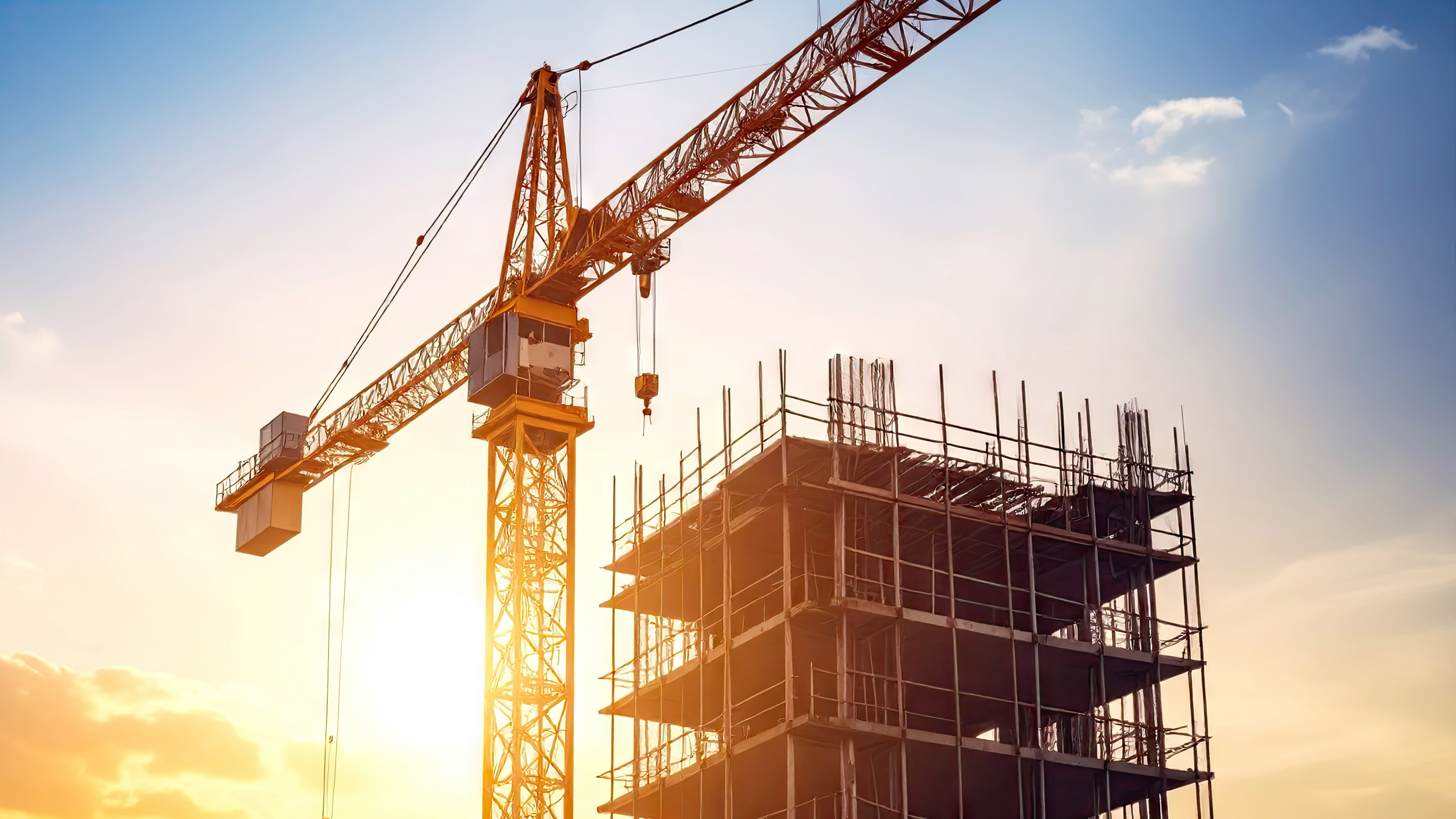 Construction Crane Arm Extending Above Half Built Tower Against A Sunset Sky