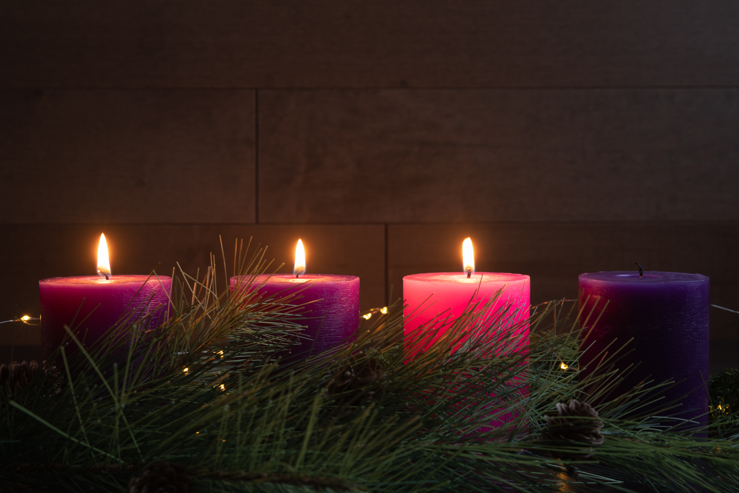 Three candles lit in advent wreath for third week of advent with pillar candles on dark wood